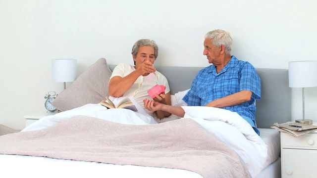 Elderly man giving a gift to his wife in bed. Great for illustrating senior lifestyle, romantic gestures, family relationships, and intimate moments. Ideal for use in health and wellness publications, blog posts about senior love and life, and advertising for bedroom or gift products.