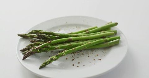 Fresh green asparagus spears on white plate with cracked pepper and sea salt