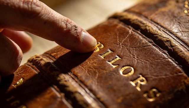 Fingertip tracing gilded letters on worn leather book spine, vintage bookbinding texture