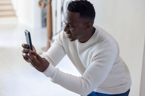 Smiling man leaning on banister using smartphone in modern home interior