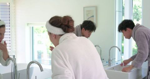 Diverse couple morning routine at double vanity in bathrobes washing face and hands