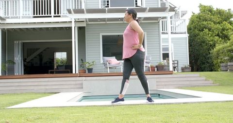 Senior woman walking along backyard pool edge for low-impact outdoor exercise and balance