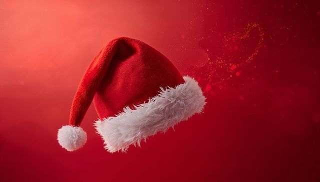 Floating Santa hat with faux-fur trim and trailing gold glitter on red gradient with festive lights