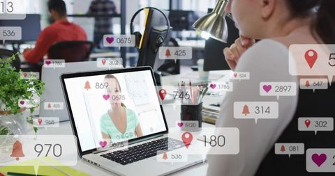 Woman watching virtual call on laptop while monitoring social engagement in modern office