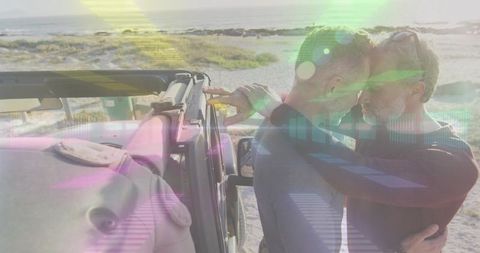 Mature male couple embracing beside jeep on sunlit coastal dune at golden hour