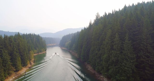 A boat navigates through a narrow waterway surrounded by dense forests, with copy space. The aerial perspective captures the serene beauty of the natural landscape and the leisure activity of boating.