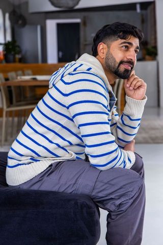 Indian man in striped hoodie sitting in cozy minimalist open-plan living space