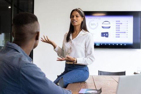 Woman leading informal presentation to coworker in modern office with mounted screen