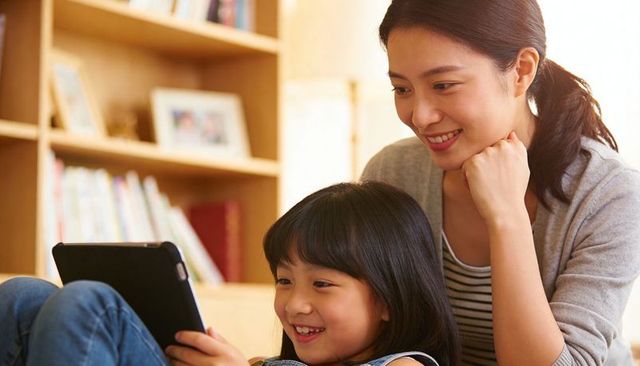 Smiling mother and daughter using tablet on couch cozy living room family bonding