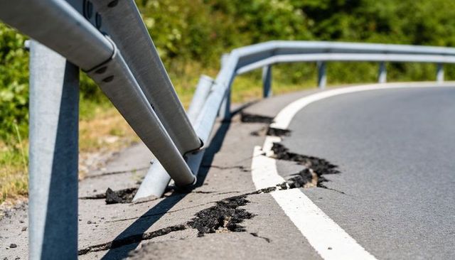 Damaged guardrail leaning over cracked asphalt on curved rural road
