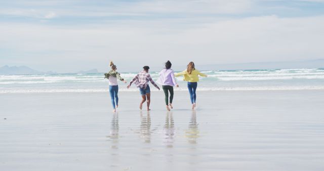 Four friends running on the beach while holding hands, enjoying a carefree summer day by the ocean. Perfect for concepts related to friendship, summer vacations, outdoor fun, happiness, and youthful exuberance. Ideal for use in lifestyle blogs, travel magazines, advertising, and social media campaigns promoting outdoor activities and bonding moments.