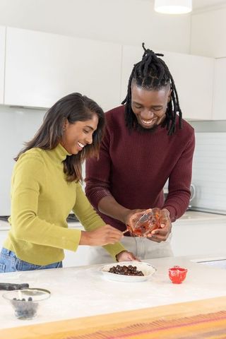 Interracial couple preparing cherry pie together on kitchen island in sunlit modern kitchen