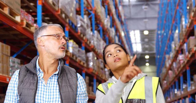 Warehouse workers collaborating in a stocked warehouse, discussing logistics and inventory management. A perfect representation for materials related to warehouse management, teamwork in industrial environments, and supply chain operations.