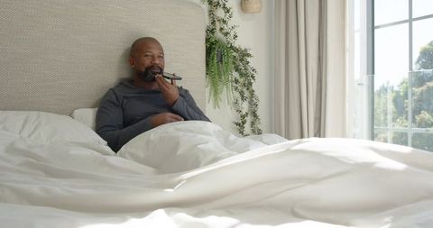African American Man Relaxing in Bed Using Smartphone Voice Feature