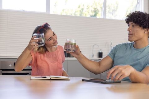 Young couple clinking water glasses with lime and berries at sunlit modern kitchen table