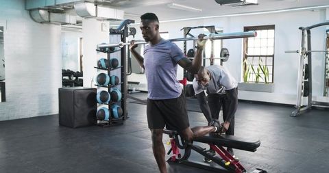Personal trainer assisting client with bulgarian squat exercise in gym setting