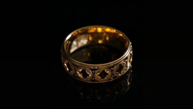 Ornate gold quatrefoil band reflecting on black surface with filigree milgrain details