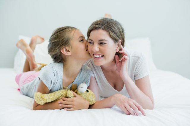 Adorable girl kissing her mother lying on a bed in bedroom at home