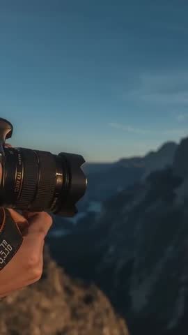 Vertical video: hands framing mountain dawn with DSLR and orange strap over scenic valley
