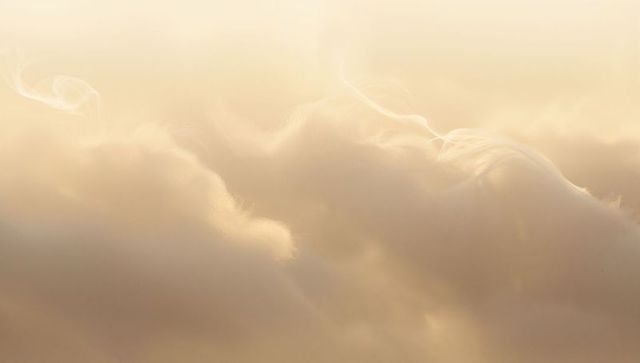 Glowing golden backlit clouds floating in soft haze, ethereal mist and wispy vapor