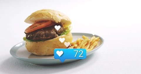 Gourmet burger with tomato and fries on pale blue-gray plate showing social like badge and floating