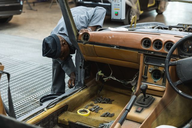 African American male mechanic working in a township workshop, bending by a car, checking and fixing cars body Workshop car mechanic profession.