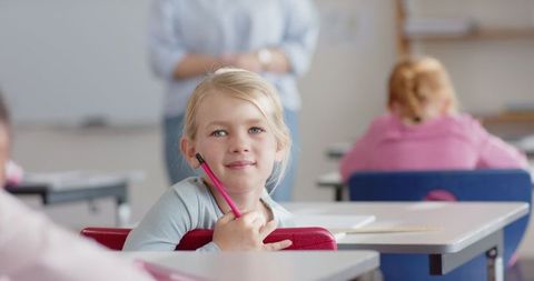 Young student smiling in class with pink pencil during lesson