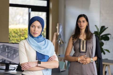 Multicultural women collaborating in office with hijab-wearing designer reviewing plans