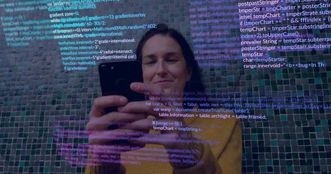 Woman holding smartphone and viewing scrolling code overlay while wearing mustard sweater