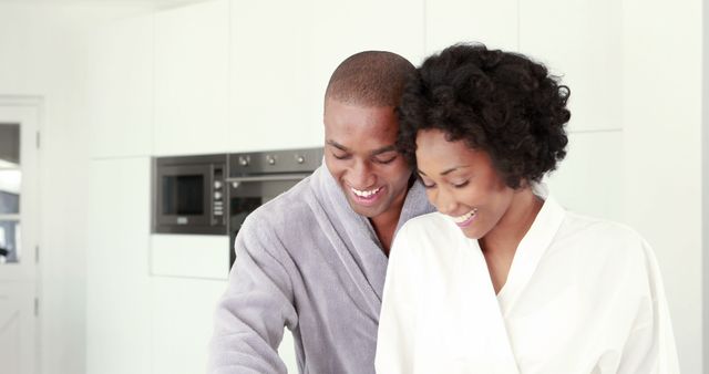 An African American couple enjoys a cozy moment together in a modern kitchen, with copy space. Their shared laughter and casual attire suggest a comfortable and intimate domestic life.