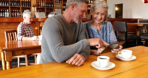Happy Seniors Enjoying Coffee and Tablet in Warm Cafeteria