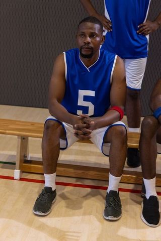 African american basketball player sitting on bench clasping hands wearing number 5 jersey