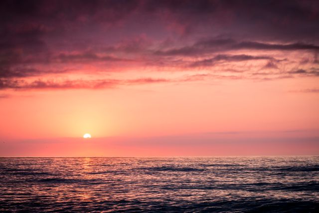 Tranquil sunset scene over calm ocean with pink and purple sky. Perfect background for websites, blogs, social media posts, and relaxation apps. Ideal for promoting travel, vacation rentals, or beachfront properties.