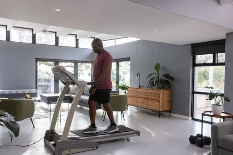 Senior man fitness walking on treadmill in modern living room
