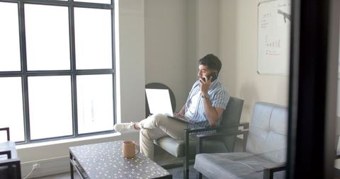Business professional combining phone call and laptop use in modern office