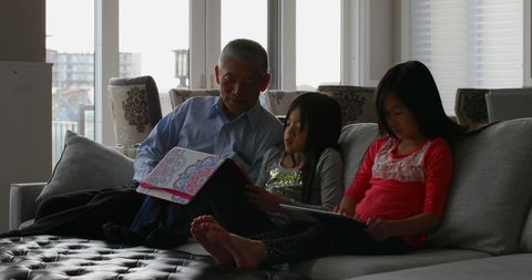Grandfather with Granddaughters Relaxing on Couch Reading Together - Download Free Stock Images Pikwizard.com