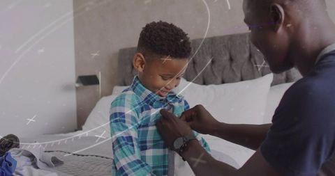 Father buttoning shirt for smiling son on bed during morning routine family bonding and care