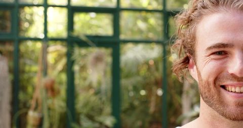 Smiling Young Man with Curly Hair in Sunlit Garden