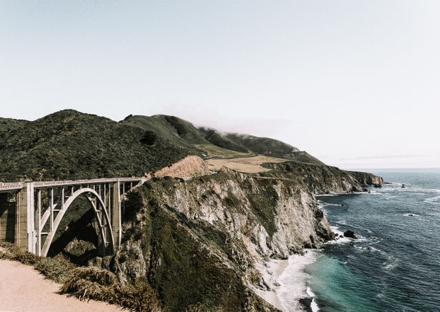 Dramatic coastal scene featuring iconic bridge and rugged cliffs meeting the ocean. Could be used for travel blogs, scenic postcards, tourism advertisements, adventure and nature publications, wallpaper backgrounds, or marketing materials showcasing beautiful and natural landmarks.