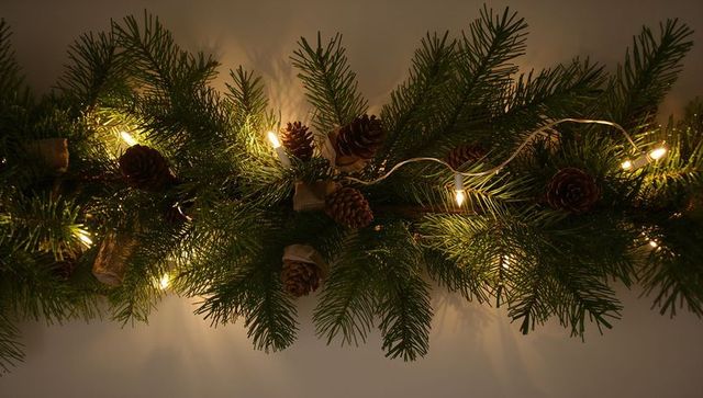 Warm rustic evergreen garland with pine cones and string lights on mantel cozy holiday decor