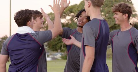 High-fiving young male athletes celebrating team victory on grass field at dusk