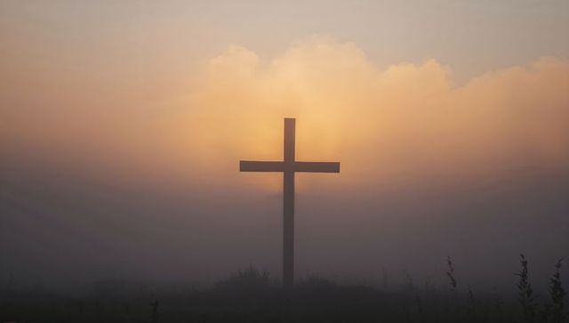 Solitary wooden cross silhouetted in sunrise fog