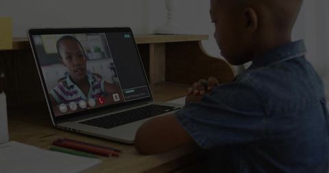 Young boy attending online class at desk with laptop, pencils and study materials