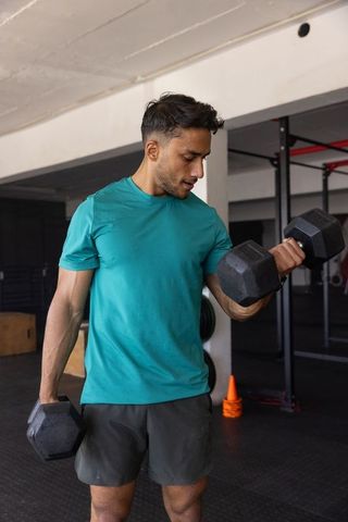 Asian man performing bicep curls with heavy dumbbells in gym during strength training