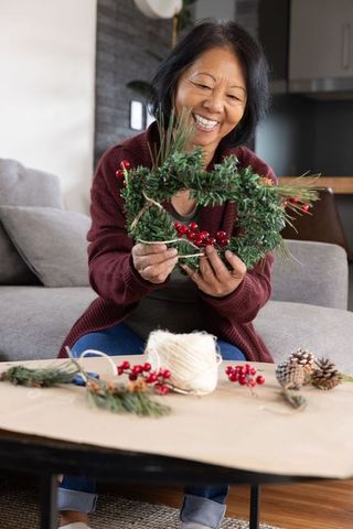 Senior asian woman crafting evergreen wreath for festive home decor