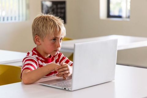 Young boy concentrating on laptop in classroom, studying online and using technology