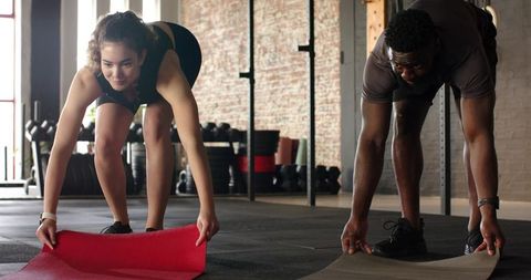 Diverse Workout Partners Unrolling Yoga Mats in Modern Gym