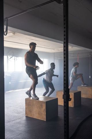 Diverse men performing plyometric box jumps in industrial gym
