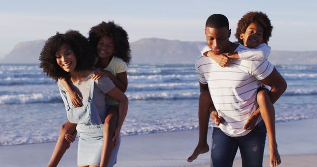 African american mother and father giving a piggyback ride to their daughter and son at the beach. family travel vacation leisure concept