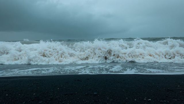 Crashing waves on black sand beach sending thick white foam under stormy sky